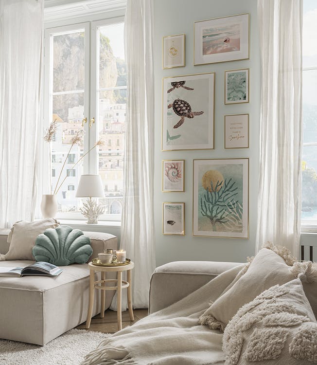 Bilderwand mit Strandpostern und Korallenpostern in Blautönen und goldenen Bilderrahmen für das Wohnzimmer.