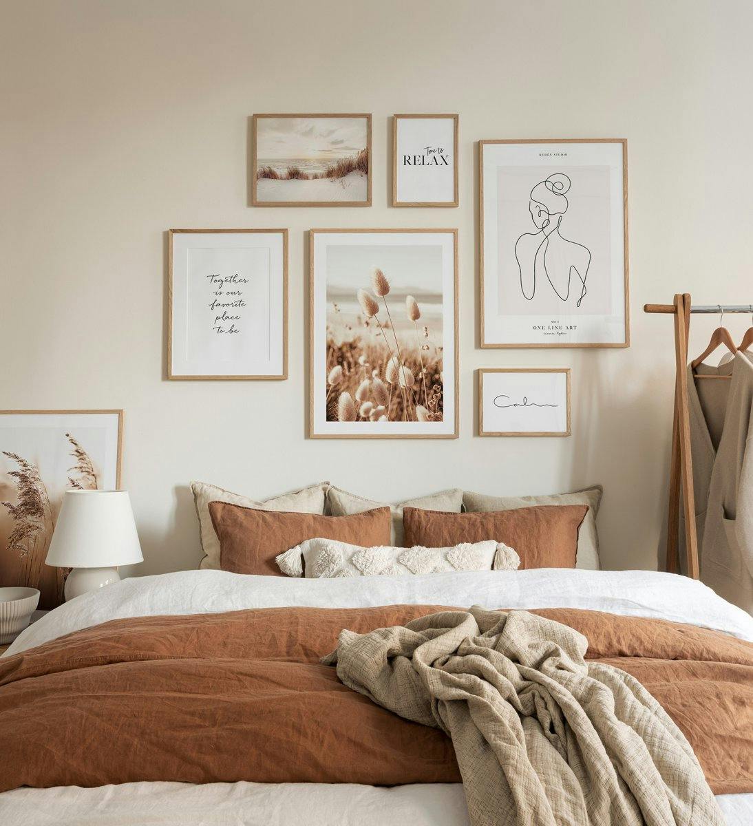 Tæt på naturgallerivæg i beige nuancer af landskabsplakater, citatprint og line art med egetræsrammer til soveværelset